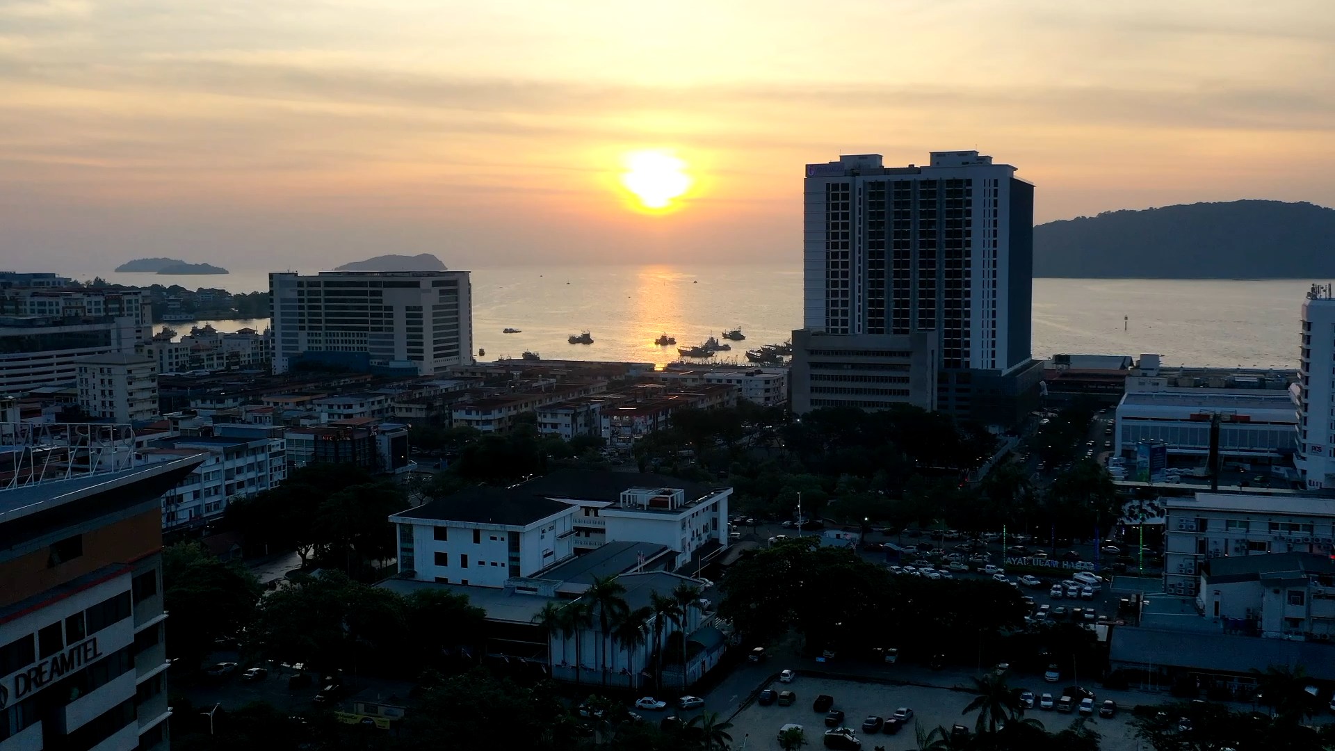 Aerial view of Kota Kinabalu at sunset, the city in the foreground and the sun setting over the sea and islands beyond
