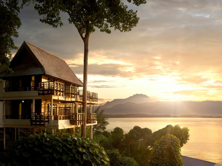 Gaya Island Resort at sunset, timber buildings set among rainforest above the bay